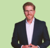 Das Foto zeigt einen Mann um die 40 Jahre, Porträt, Blazer, weißes Hemd, rotblonde Haare, Bart, Brille, er lächelt. Er steht vor einem grünen Hintergrund. Es handelt sich um Leonardo Mallmann, CEO Chiesi Deutschland. Es ist ein Porträt über ihn und seine wertebasierte Führung mit Nachhaltigkeitszielen