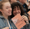 Roche Content Creator Masterclass 2025: Das Bild zeigt zwei junge Frauen auf der Veranstltung, die lachend ein Heft mit CCMC-Logo in die Kamera halten.
