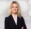 Porträt Frau mit langen blonden Haaren, leicht lächelnd, Ende 30, schwarzer Blazer, weiße Bluse, Business-Pose. Es handelt sich um Kathleen Rieser